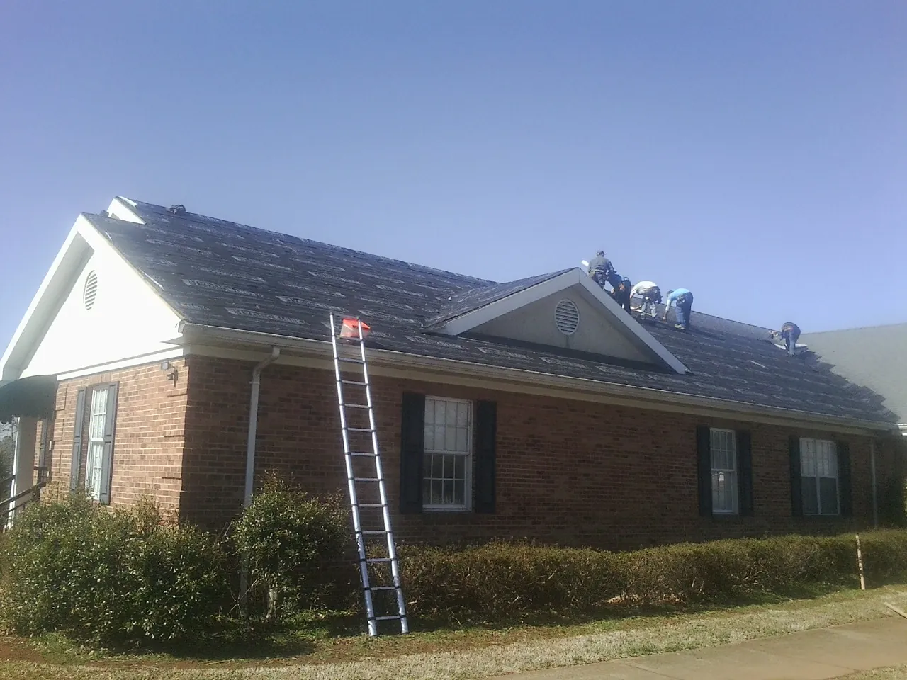 Crew tearing shingles off a brick ranch roof with a ladder set — Metal Roof Repair work by our crew in Ochlocknee