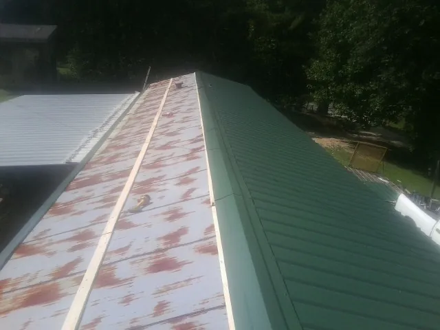 Old rusted panels beside newly installed green metal roofing — Wind Damage Roof Repair by Roofing Brothers in Ochlocknee