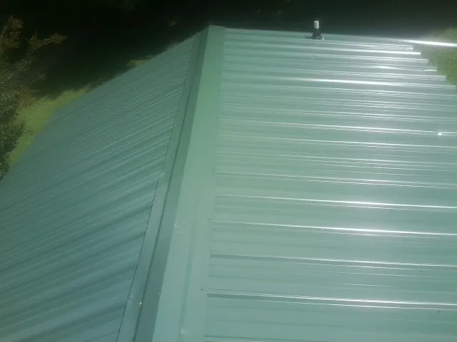 New green metal panels meeting at the ridge of a roof — Flat Roof Repair work by our crew in Ochlocknee