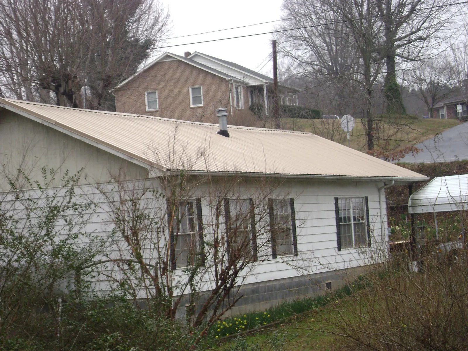 Tan metal roof on a white sided house set into a hillside — Commercial Roofing by Roofing Brothers in Ochlocknee